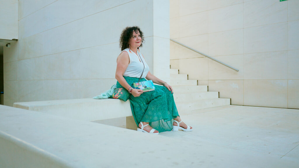 La escritora Mar Montilla posando con su libro "El secreto de Adela" sentada en un banco de piedra blanca