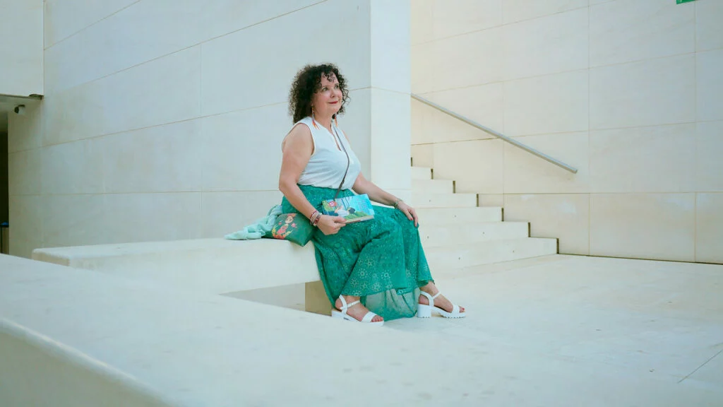 La escritora Mar Montilla posando con su libro "El secreto de Adela" sentada en un banco de piedra blanca