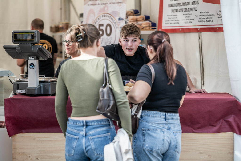 Un joven comerciante atendiendo a dos turistas en el Mercat de Mercats