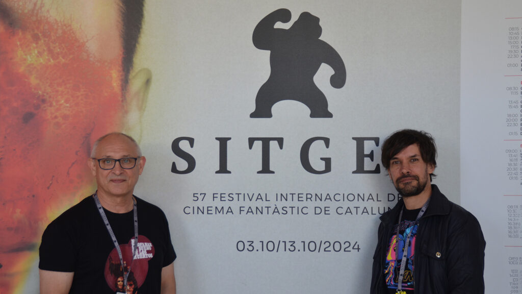 Mario Herrera y Santi Serrano, de Pánico en la sala, frente al cartel de la presente edición del Festival de Sitges.