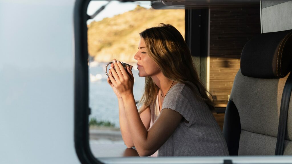 Una mujer disfruta de una taza de café caliente mientras disfruta de unas preciosas vistas dentro de su caravana. Fotografía de Freepik