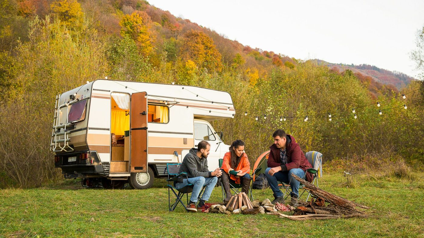 Un grupo de amigos disfrutan del atardecer frente a su autocaravana. Fotografía de Freepik.