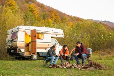 Un grupo de amigos disfrutan del atardecer frente a su autocaravana. Fotografía de Freepik.