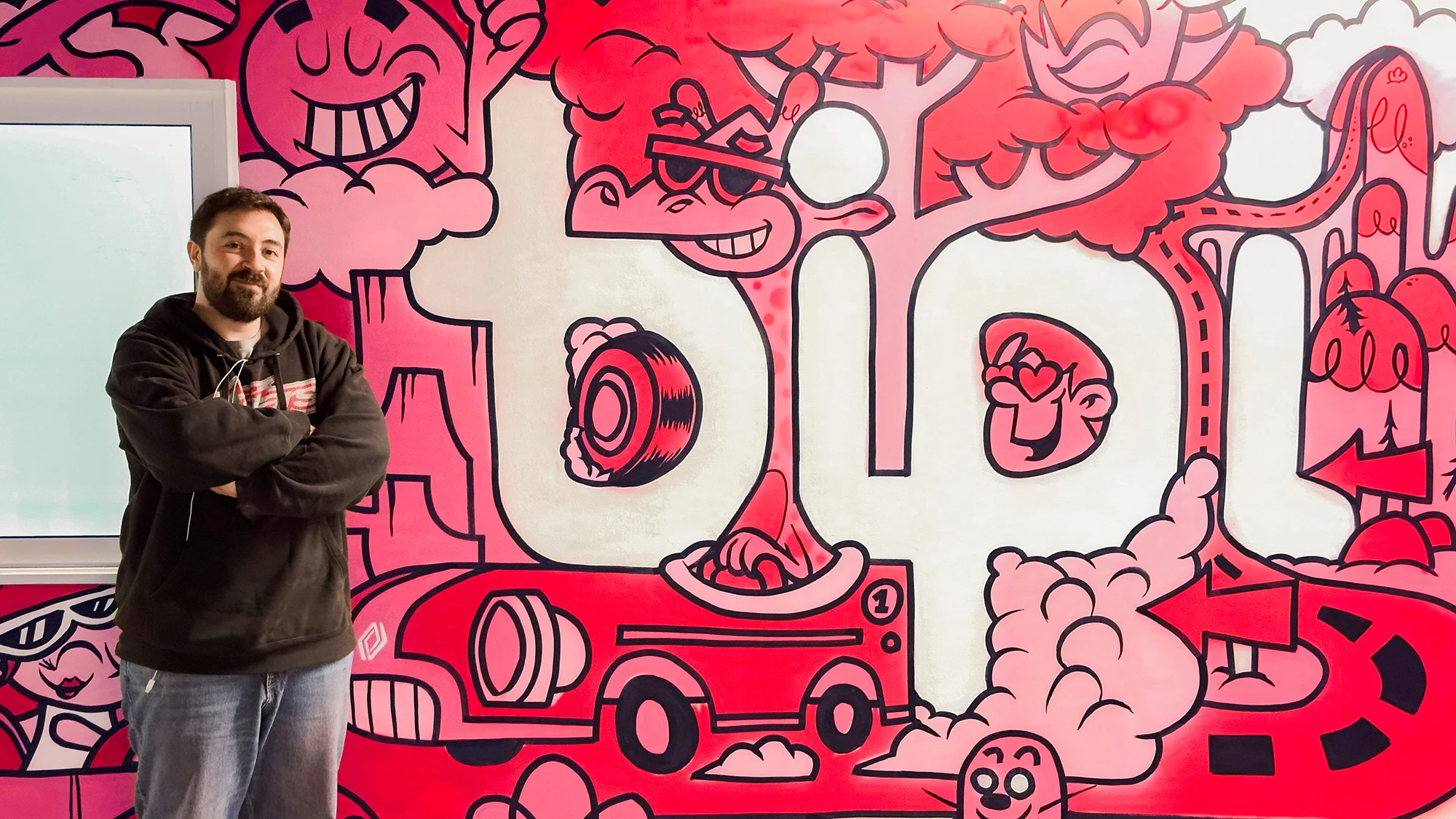 El artista ilustrador Moñuz en una fotografía promocional junto a su mural de Bipi