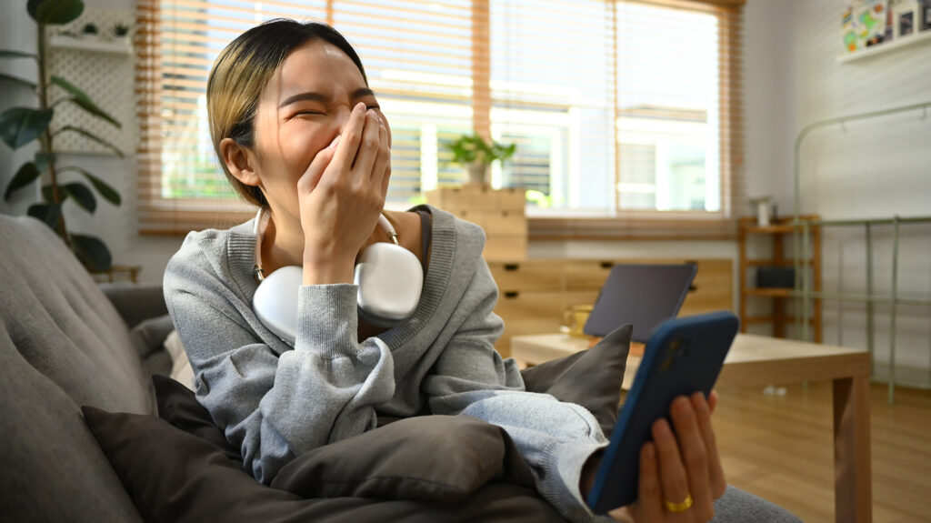 Mujer riendo tras escuchar una broma en un podcast. Fotografía Envato