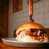 Hamburguesa de costilla de Angus cocinada a baja temperatura y lacada con miel y kimchi, acompañada de cebolla encurtida y alioli de azafrán y cilantro