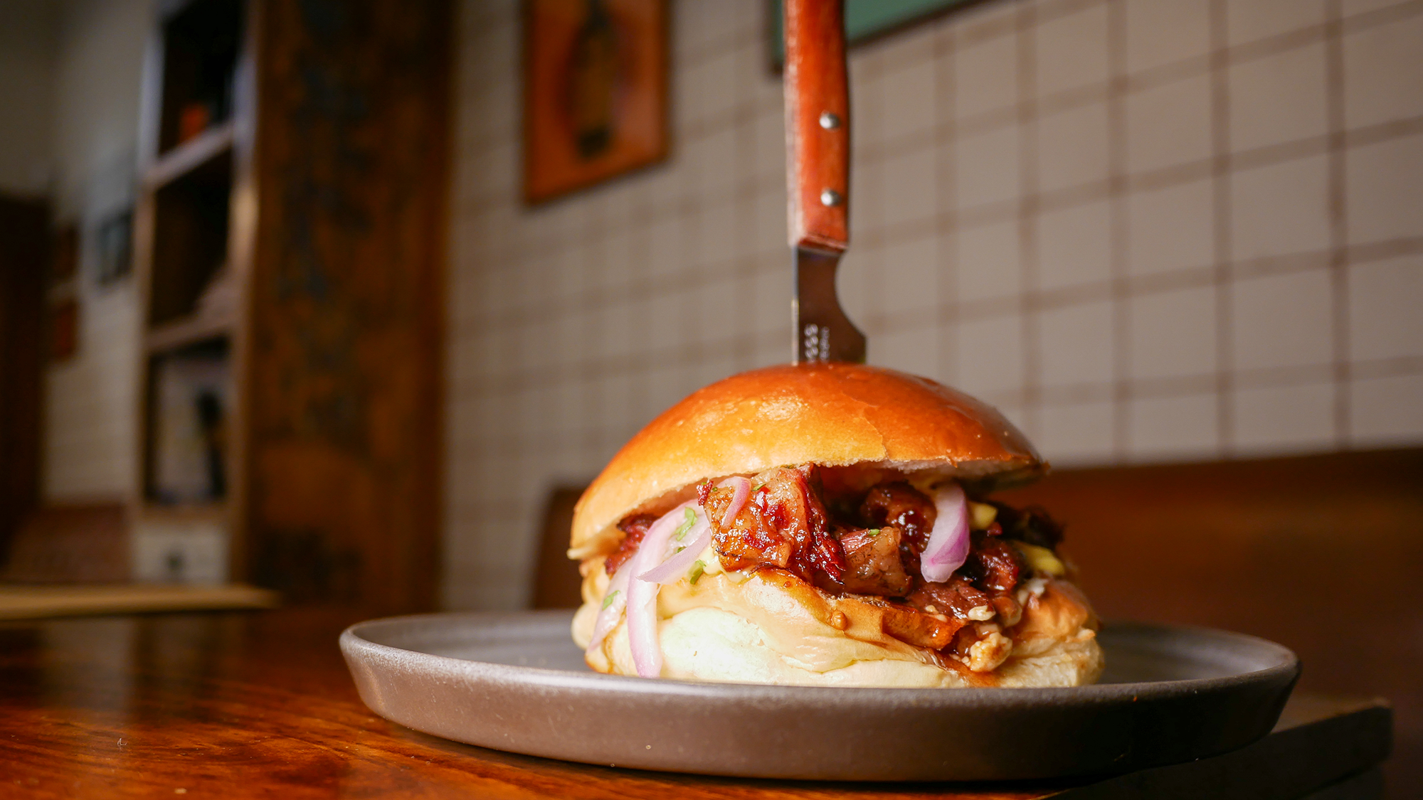 Hamburguesa de costilla de Angus cocinada a baja temperatura y lacada con miel y kimchi, acompañada de cebolla encurtida y alioli de azafrán y cilantro